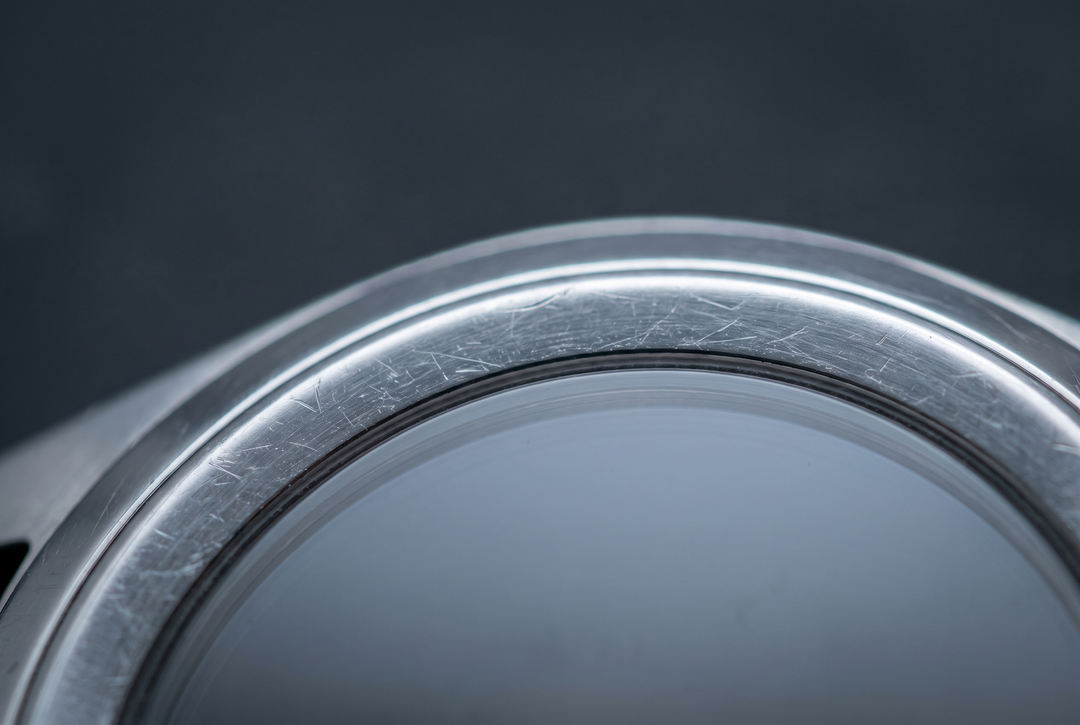 Macro de la tranche polie d'un boîtier en acier révélant de fines micro-rayures sous la lumière